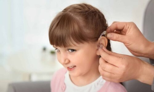 ילדה עם מכשיר שמיעה מקבלת סיוע מהורה – קצבת ילד נכה לליקוי שמיעה